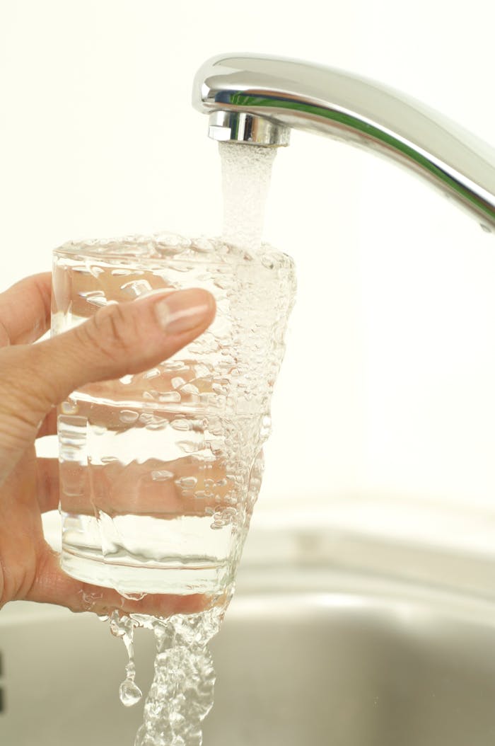 Close-up of a hand holding a glass as tap water fills it, promoting cleanliness and freshness.